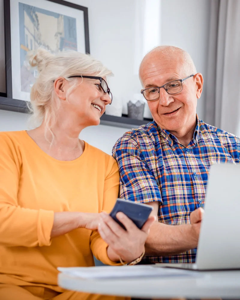 An older couple smiling together at a table with a laptop and phone