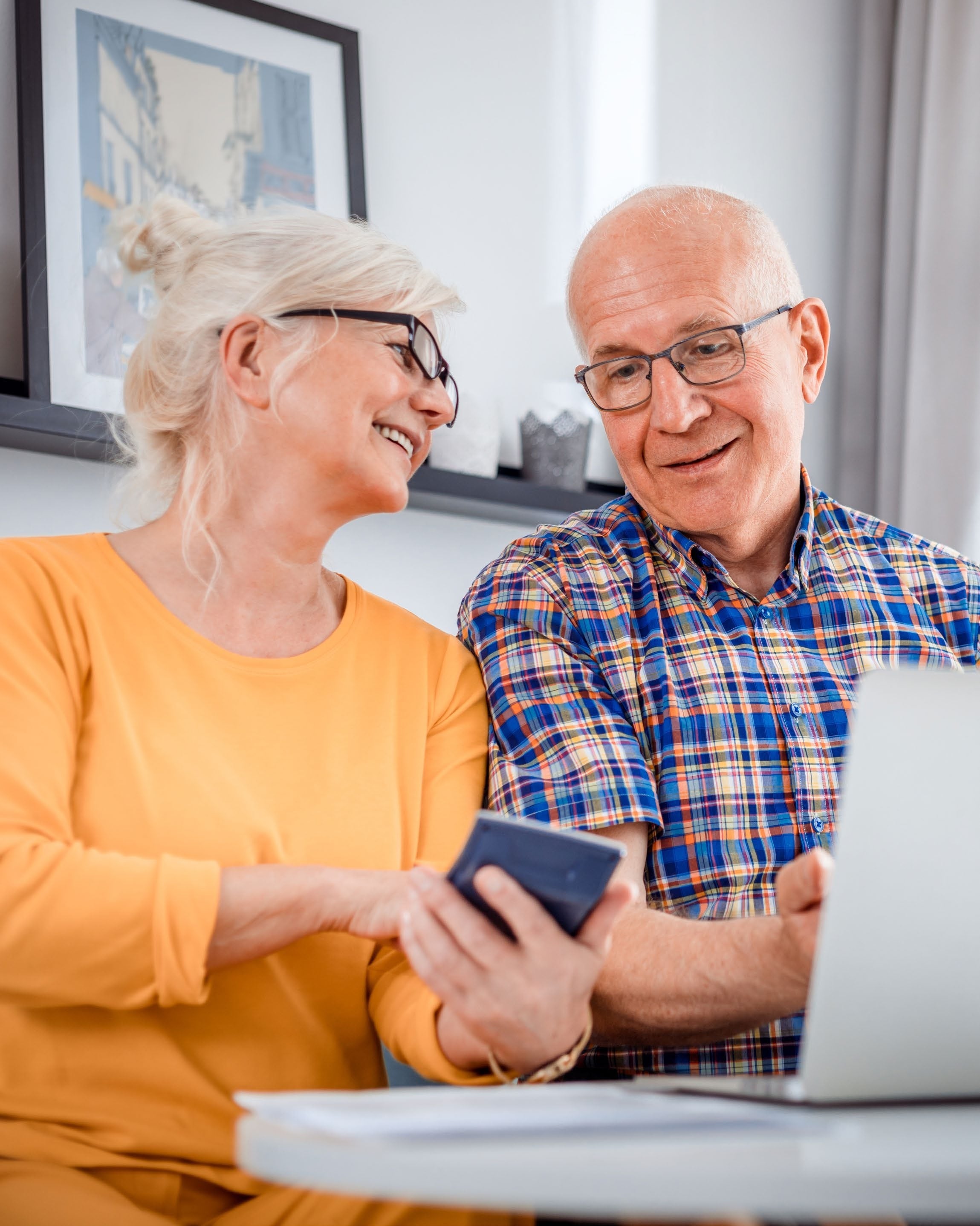 An older couple smiling together at a table with a laptop and phone