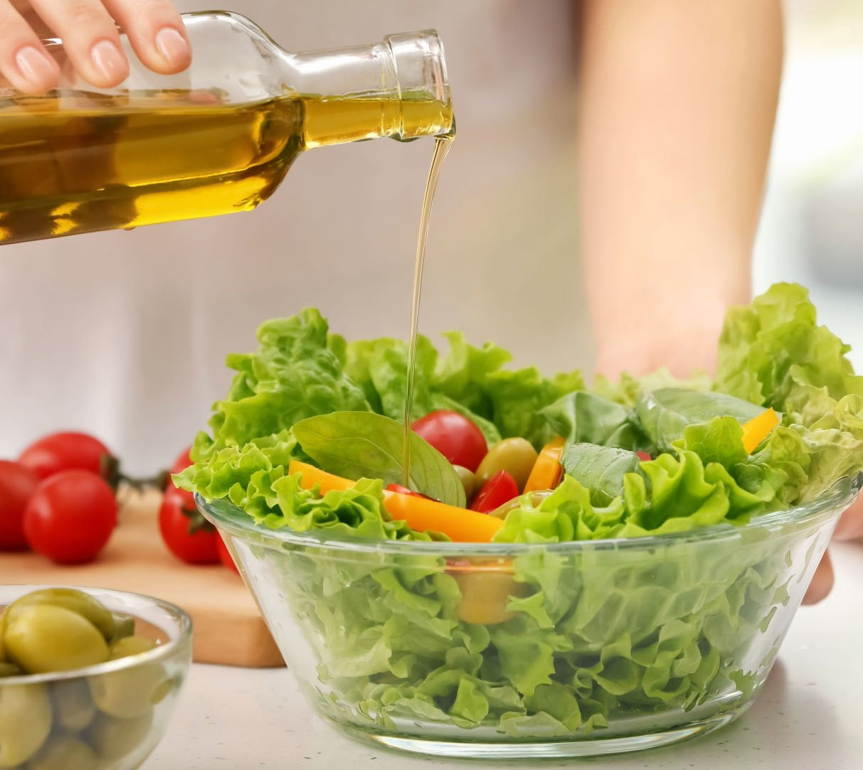 Olive oil being poured over a fresh salad with lettuce, tomatoes and yellow peppers