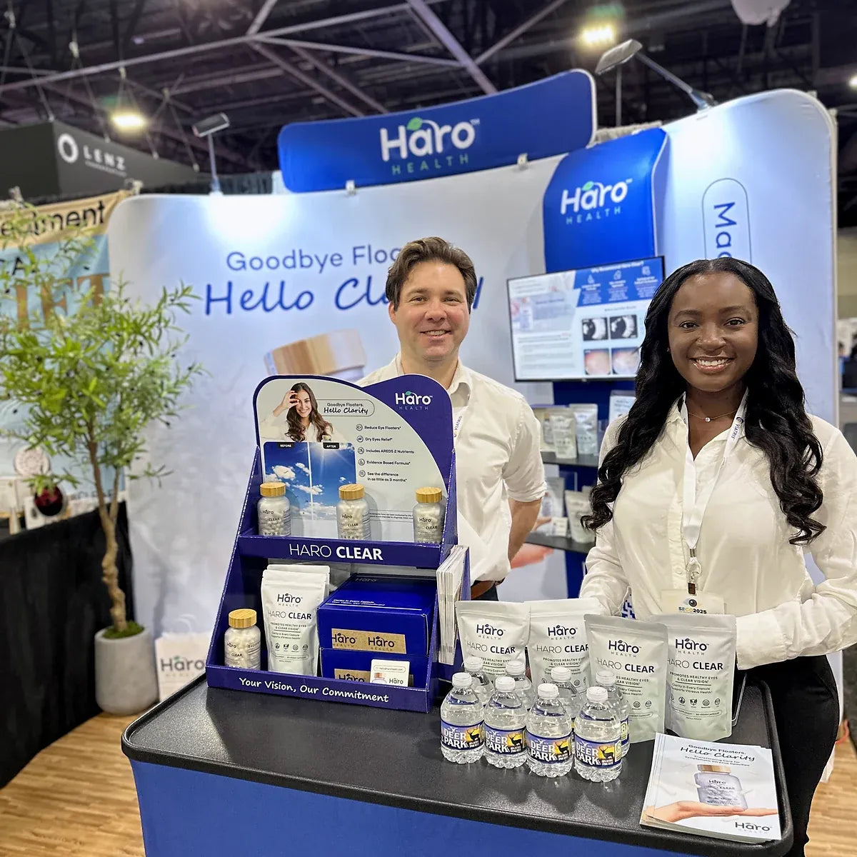 Two smiling people behind a Haro Health conference display with bottles and refill pouches