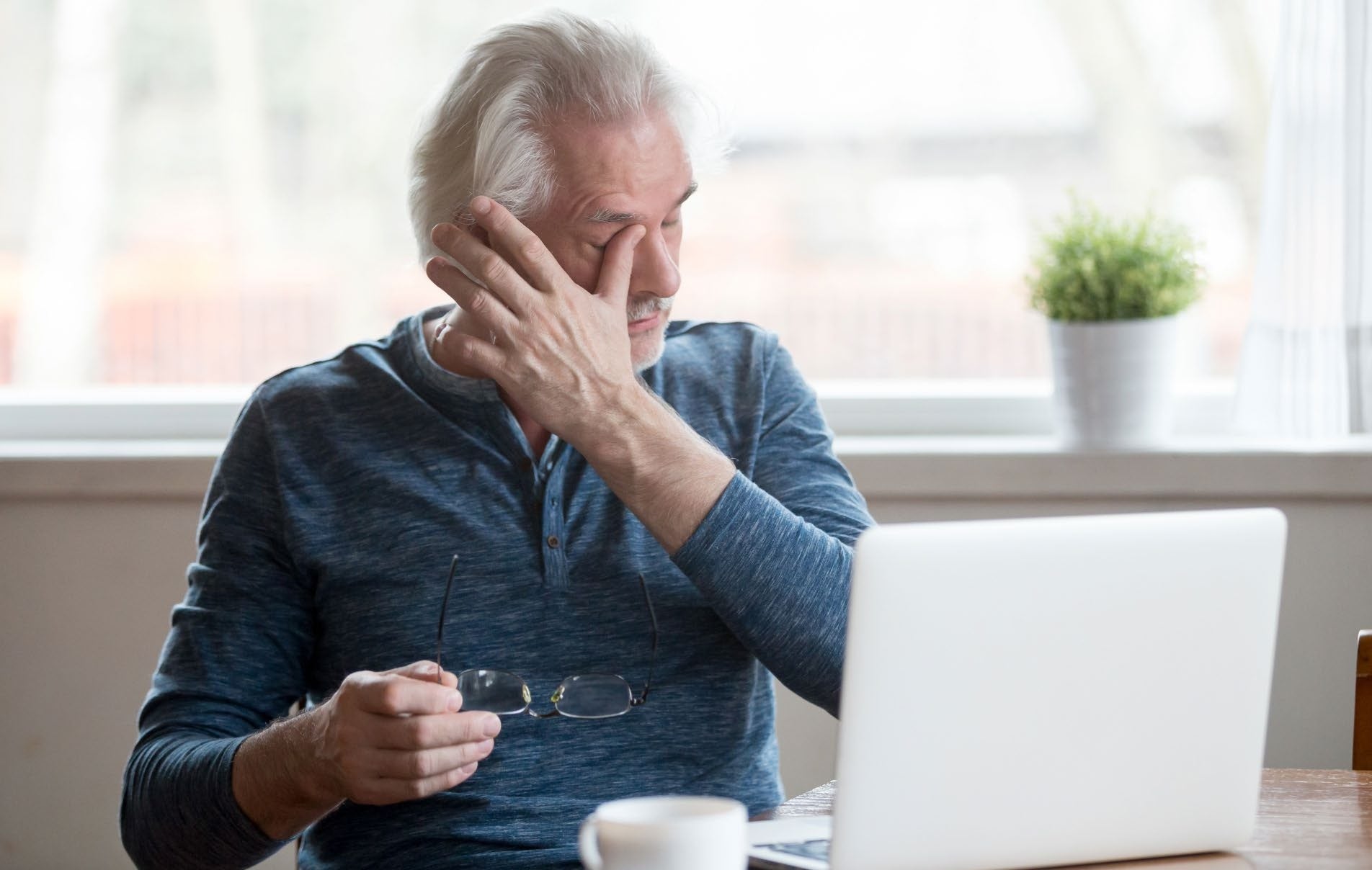 An older man taking a break from his laptop with his glasses in his hand