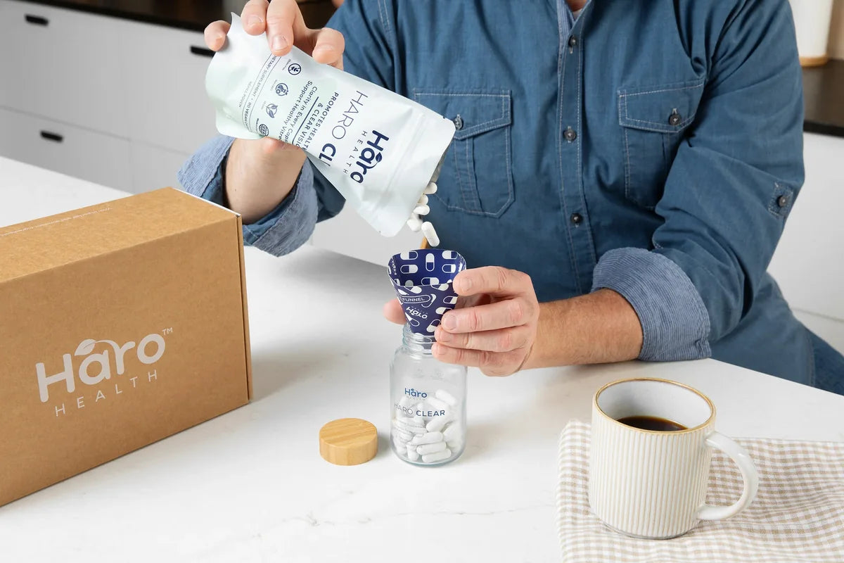 A person refilling the Haro Clear glass bottle using the pouch and funnel at a kitchen counter