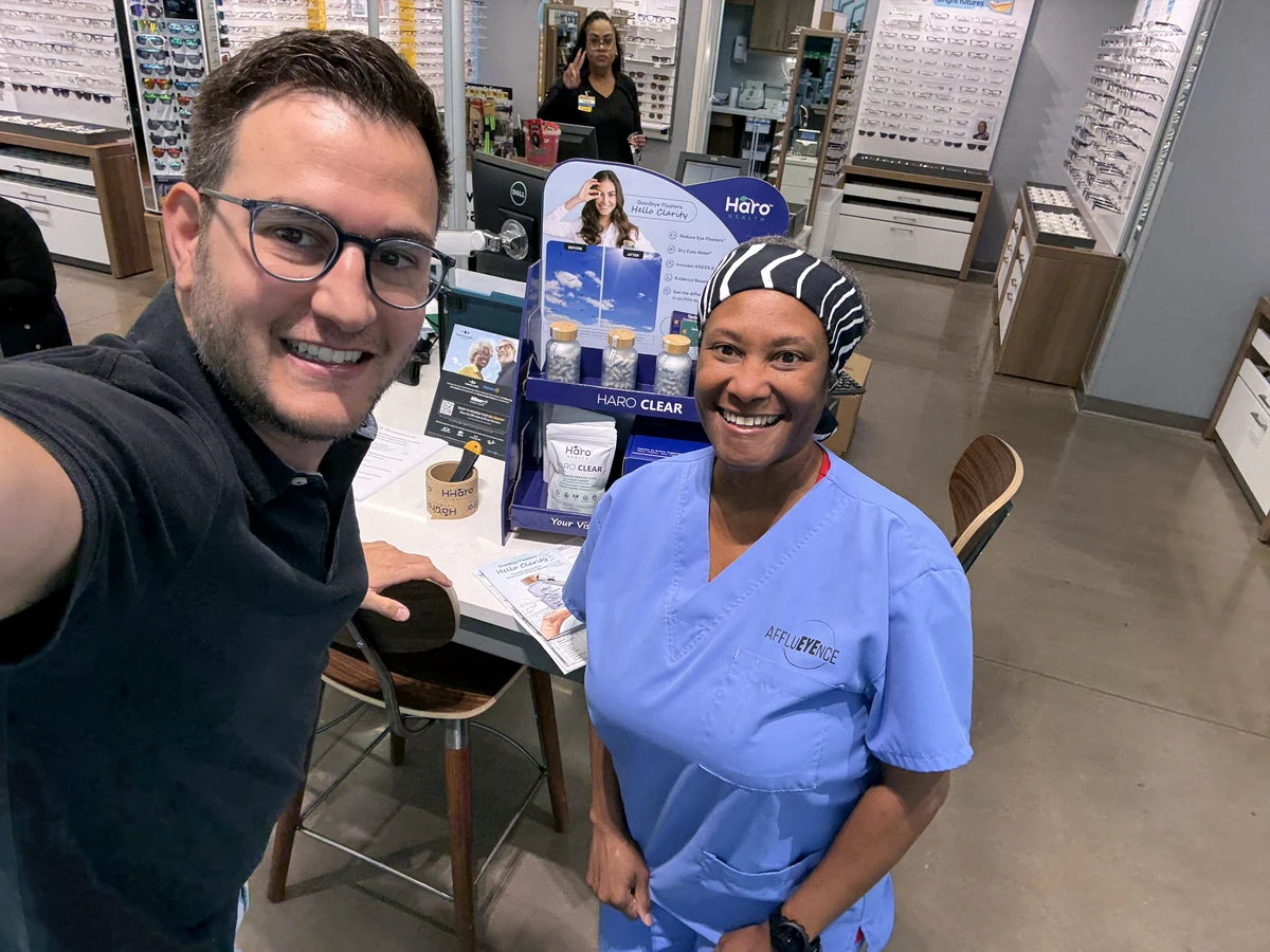 Two people beside a Haro Clear display in an optical clinic